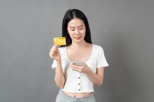 mulher asiática com cara feliz e apresentando cartão de crédito na mão, mostrando confiança e segurança para fazer o pagamento foto