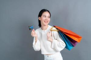 linda mulher asiática com sacolas de compras e apresentando cartão de crédito foto
