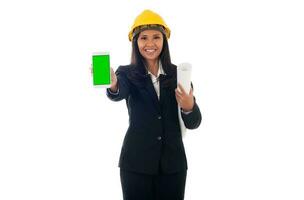 retrato do misturado raça ásia engenheiro mulher com capacete segurando plantas e mostrando verde tela Móvel telefone isolado branco fundo foto