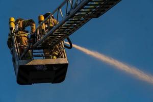 bombeiros subindo escada contra prédio e apagando um incêndio foto
