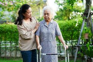 cuidador ajuda paciente idosa asiática com deficiência andar com caminhante no parque, conceito médico. foto