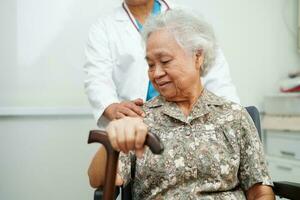 médico Socorro ásia idosos incapacidade mulher paciente segurando caminhando bastão dentro enrugado mão às hospital. foto