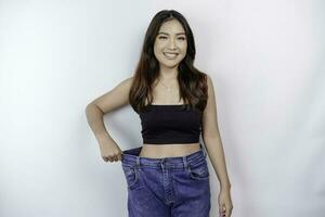 dieta e peso perda conceito. uma jovem ásia mulher dentro de grandes dimensões jeans isolado em uma branco fundo. foto