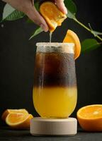gelado café com laranja suco dentro uma transparente vidro, uma mulher mão aperta a laranja fatia para dentro uma bolha beber foto