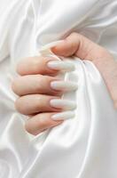 uma mulher mãos com uma manicure em eles, a unhas estão pintado dentro uma branco cor. foto