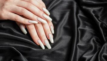 uma mulher mãos com uma manicure em eles, a unhas estão pintado dentro uma branco cor. foto