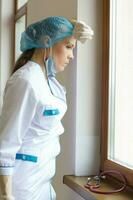 jovem cirurgião depois de uma trabalhando dia permanece fechar para a janela dentro a clínica corredor foto