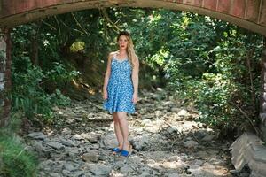 uma jovem bonita mulher com uma azul vestir debaixo uma ponte arco foto