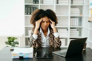 africano mulher quem é cansado e pensar demasiado a partir de trabalhando com tábua e computador portátil às escritório. foto