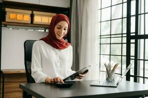 jovem árabe fêmea empreendedor vestindo uma hijab trabalhando conectados com uma computador portátil às escritório foto