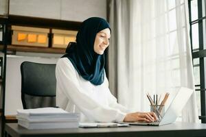 jovem árabe fêmea empreendedor vestindo uma hijab trabalhando conectados com uma computador portátil às escritório foto