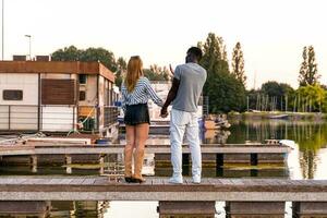 jovem multirracial amoroso casal segurando mãos em uma cais do uma rio porta foto