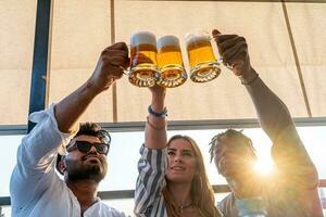 pequeno grupo do jovem adulto multiétnico amigos brindar com três canecas do Cerveja foto