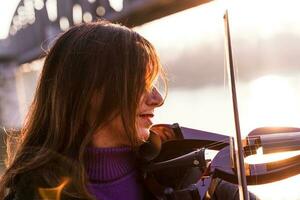 atraente meio envelhecido mulher jogando a elétrico violino ao ar livre foto