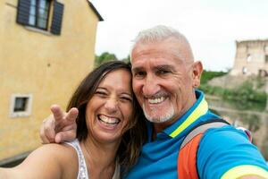 lindo meio envelhecido casal levando uma selfie dentro a ruas do uma agradável italiano Vila foto