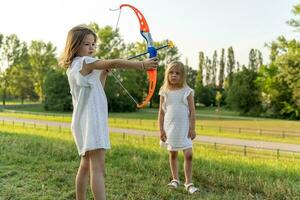 fofa pequeno menina é jogando com uma brinquedo arco e seta com dela irmã foto