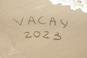 palavra vacay 2023 escrito em a areia foto