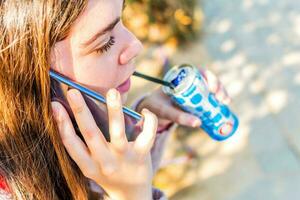 jovem mulher usando dela célula telefone e bebendo uma refrigerante, dentro a parque foto