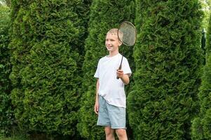 uma feliz Garoto detém uma badminton raquete dentro dele mãos, ao ar livre Atividades foto