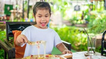 ásia menina vestindo branco camisa segurando triângulo forma inoxidável aço pá colher peça do delicioso saboroso havaiano tradicional italiano crosta fino crocantes presunto e abacaxi pizza acima alongamento queijo foto