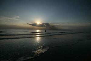 a beleza do a pôr do sol em a de praia com a silhueta do uma pescador foto