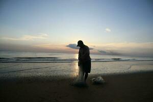 a beleza do a pôr do sol em a de praia com a silhueta do uma pescador foto