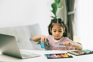 fofa pequeno ásia menina usando computador portátil às lar. Educação conceito. foto