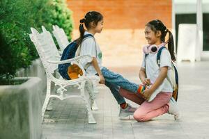 dois pequeno meninas sentado em uma Banco dentro a parque e conversando. foto