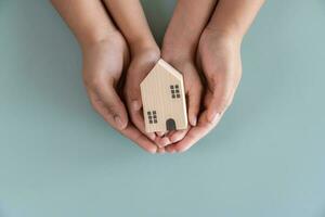 mãos segurando pequeno de madeira casa conceito do proteção ou salvando para comprando Novo vivo área. conceito e tema para empréstimo e investimento. foto