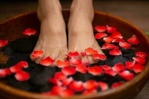 mulher encharca dela pés dentro uma tigela com flor pétalas foto