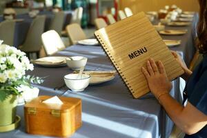 uma tailandês mulher dentro uma restaurante enquanto esperando para amigos para ter jantar junto. ela escolhe uma cardápio e ordens Comida este ela e dela amigos gostar antes amigos chegar tão elas pode comer. foto