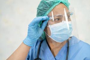 médico asiático usando protetor facial e terno novo normal para verificar o paciente protege a segurança infecção covid-19 surto de coronavírus na enfermaria de quarentena do hospital.