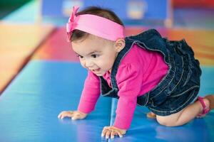 lindo dez meses bebê menina rastejando em uma colorida fundo. cedo estimulação para crianças conceito. foto