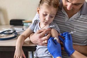 uma menina com o pai no consultório médico da clínica está sendo vacinada contra o coronavírus. o conceito de vacinação, imunização, prevenção contra covid-19.