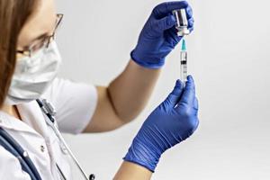 uma médica usando uma máscara médica injeta a vacina contra o coronavírus em uma seringa na clínica. O conceito de vacinação, imunização, prevenção contra covid-19.