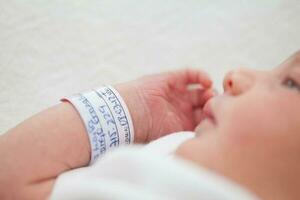 fechar-se do uma recém-nascido braço e pulseira às hospital em a dia do dela nascimento foto