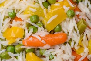 delicioso fresco branco fervido arroz com legumes cenouras, pimentas e espargos feijões em uma cerâmico prato foto