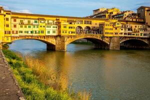 dourado hora às a ponte vecchio uma medieval pedra tímpano fechado segmento arco ponte sobre a Arno rio dentro Florença foto