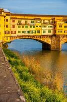 dourado hora às a ponte vecchio uma medieval pedra tímpano fechado segmento arco ponte sobre a Arno rio dentro Florença foto
