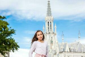 lindo jovem menina às a rio avenida dentro frente do a famoso gótico Igreja do la ermita construído em 1602 dentro a cidade do cali dentro Colômbia foto