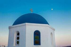 tradicional cúpula do a igrejas às oia cidade e a lua dentro santorini ilha foto