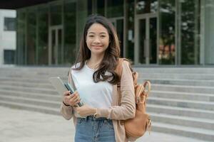 bela estudante mulher asiática com mochila e livros ao ar livre. menina sorriso feliz carregando um monte de livro no campus da faculdade. retrato feminino na universidade internacional da ásia. educação, estudo, escola foto