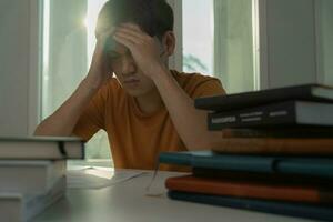 homem estudante asiático tem ansiedade por causa dos exames, o homem se prepara para o teste e aprende lições na biblioteca. estresse, desespero, pressa, leitura mal-entendida, desencorajado, expectativa, conhecimento, cansado foto