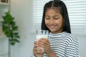 crianças mulheres bebem leite para nutrir o corpo e nutrir o cérebro. menina jovem asiática aprende em casa. menina feliz bebe leite e lê um livro para exame, homeschool. educação, vitaminas, desenvolvimento foto