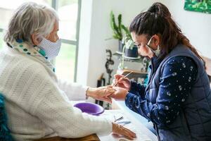 Senior mulher obtendo uma manicure às casa durante cobiçado 19 pandemia vestindo face mascarar foto