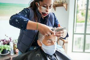 Senior mulher obtendo uma corte de cabelo às casa durante covid19 pandemia vestindo face mascarar foto