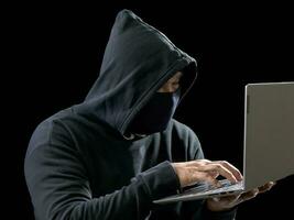 hacker espião homem uma pessoa com capuz preto sentado em uma mesa olhando computador laptop usado segurança de ataque de senha de login para circular dados digitais no sistema de rede da internet, fundo escuro noturno. foto