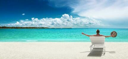 homem com chapéu sentado em uma área coberta cadeira em ensolarado de praia. foto
