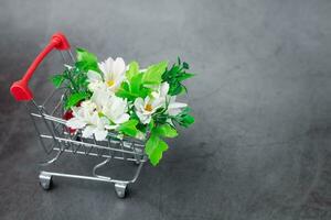 uma falso grupo do flores dentro uma mimi compras carrinho em Sombrio fundo foto