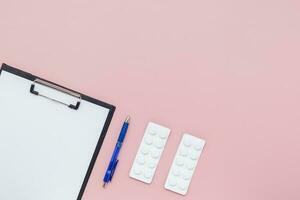 plano deitar do prancheta com papel, azul caneta e bolha pacote do remédio comprimido em Rosa fundo foto